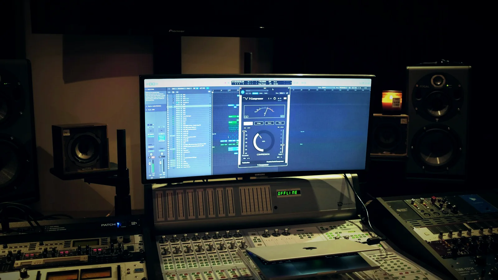 A dark studio with a monitor, mixing desks and speakers, and a lit candle in the corner